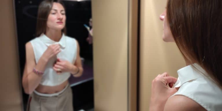 Eine Frau ajustiert ihren Blusenkragen und schaut in den Spiegel
