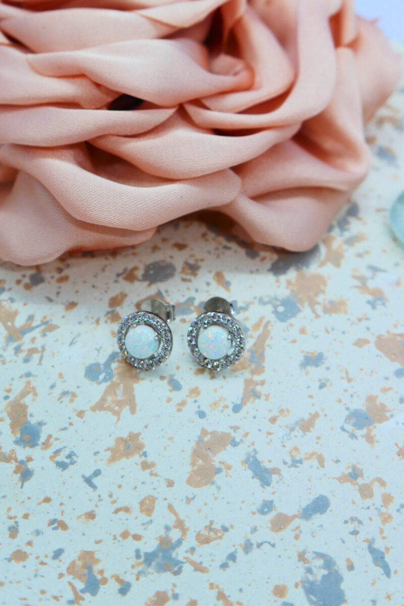 Ohrstecker aus 925 Sterlingsilber mit rundem, weißen Opal und einem Ring aus Zirkonia, gestylt auf Tablett mit Kunstrose